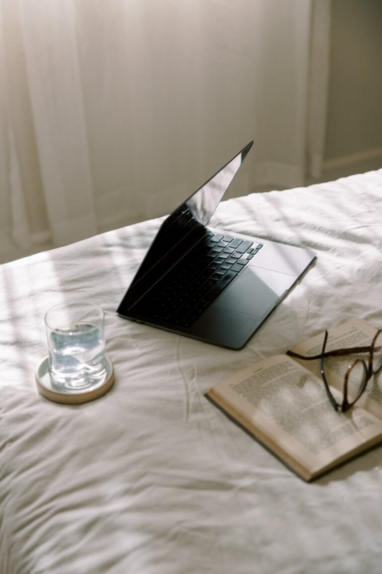 An open laptop on a bed beside a glass of water