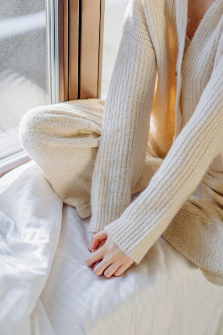 Person wrapped in a cream knit sweater with hands tucked into the sleeves, in soft morning light