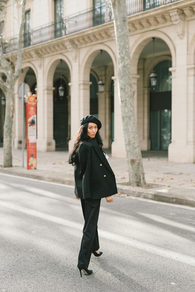 Woman in a black coat and beret walking along a European city street