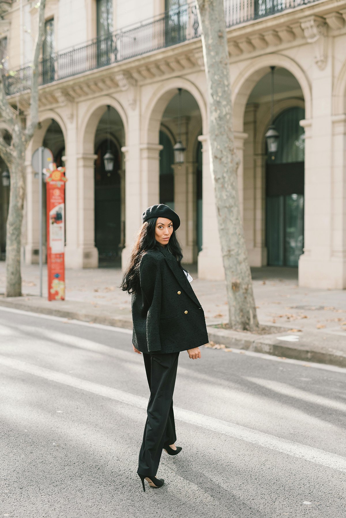 Woman in a black coat and beret walking along a European city street