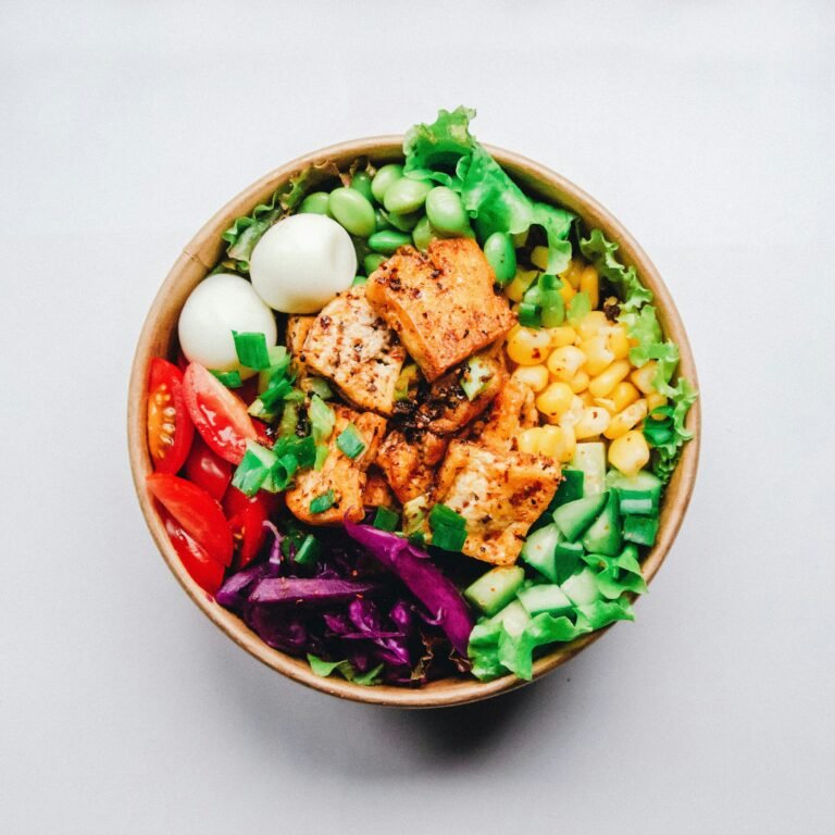 A colorful grain bowl with salmon, chickpeas, cucumber, tomato, red cabbage and a soft-boiled egg