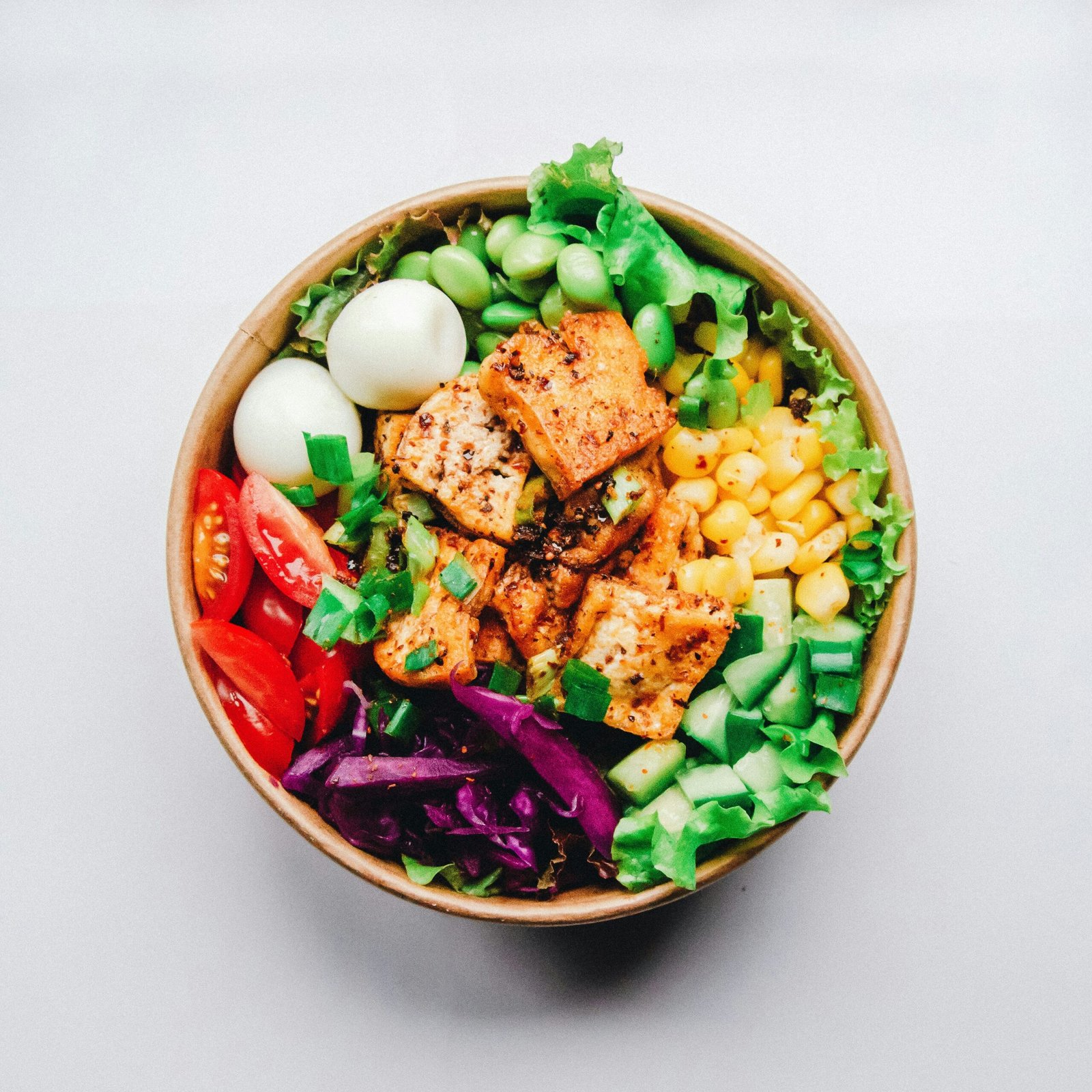 A colorful grain bowl with salmon, chickpeas, cucumber, tomato, red cabbage and a soft-boiled egg