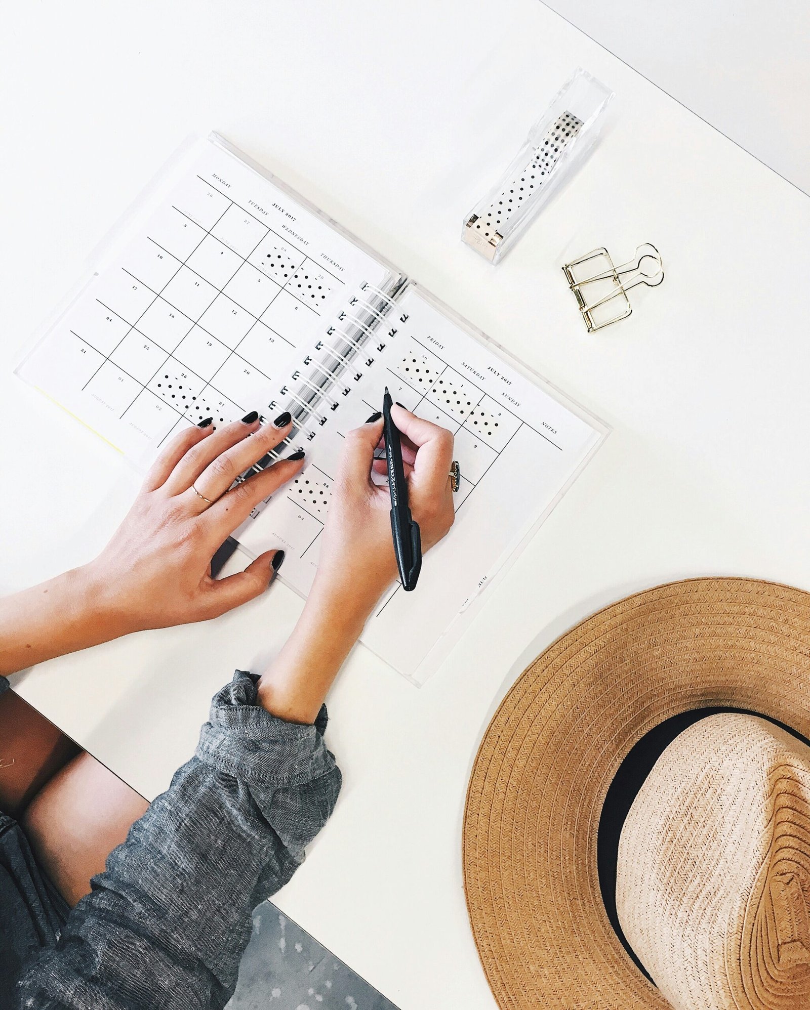 Overhead shot of hands writing in a planner on a table, with a straw hat nearby
