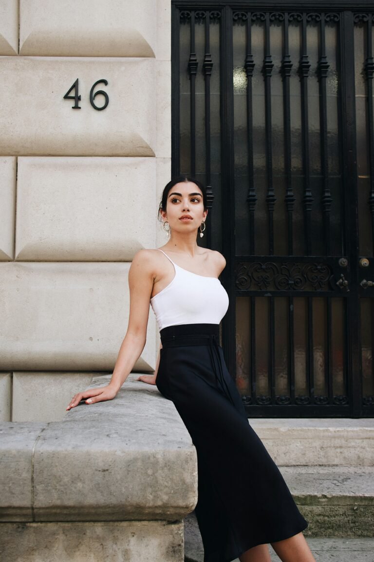 Woman in a white top and black skirt sitting against a dark railing, looking confident
