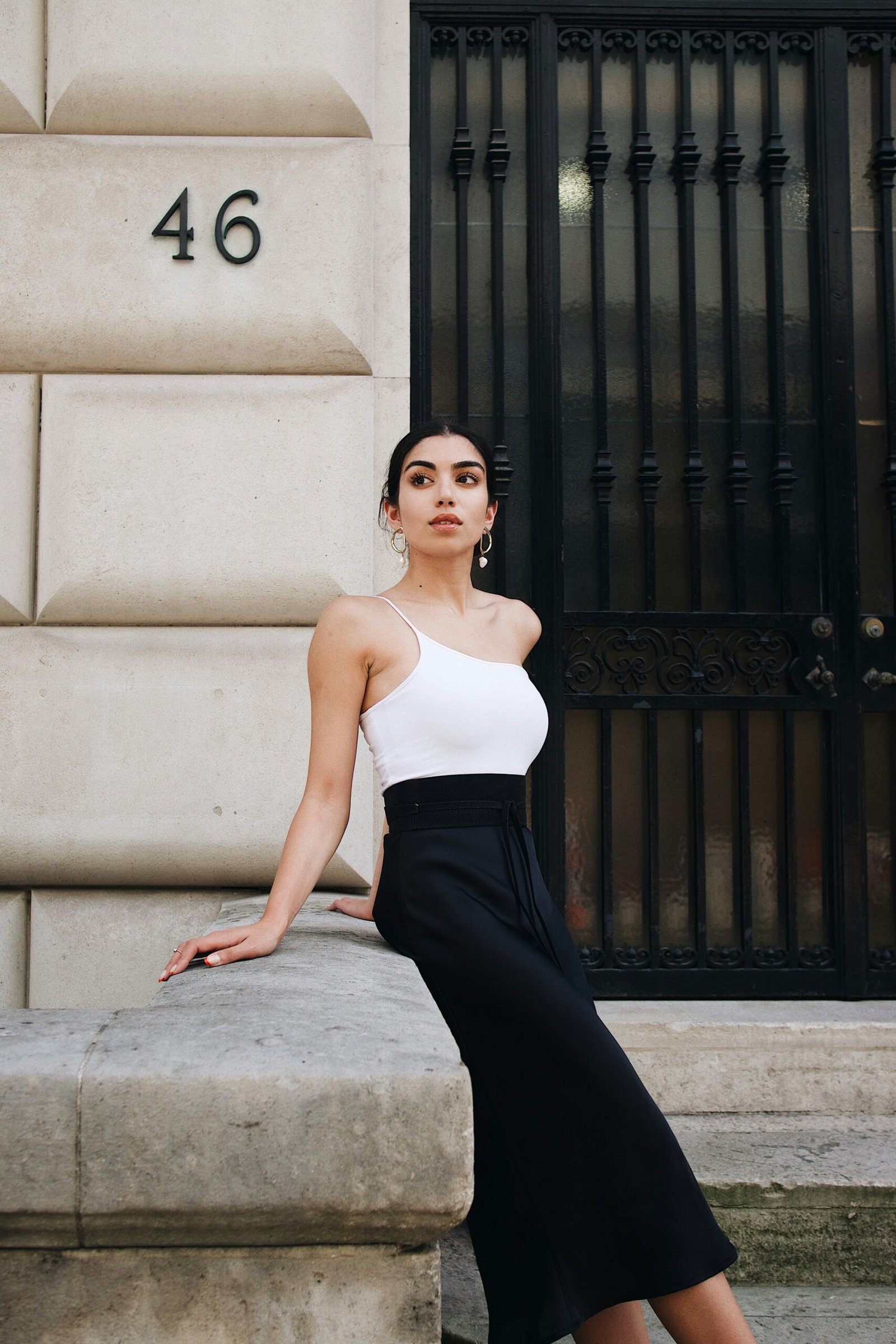 Woman in a white top and black skirt sitting against a dark railing, looking confident