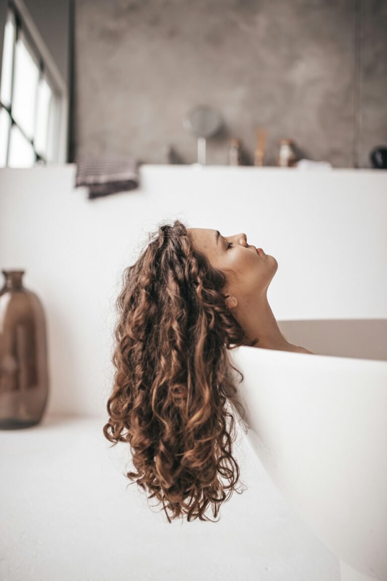 Woman with curly hair leaning her head back in a bathtub, hair flowing over the edge